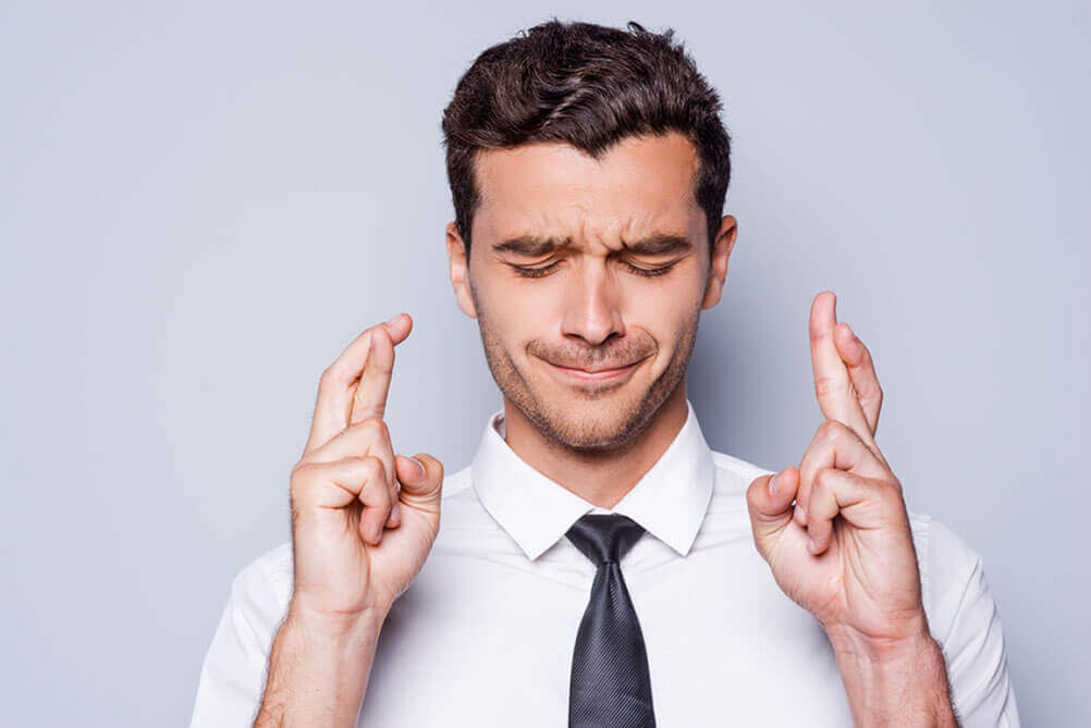 Man with closed eyes crossing fingers of both hands