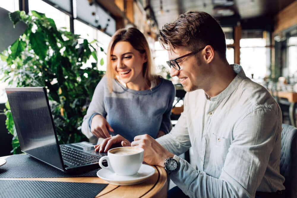 Couple drinking coffee in front of open laptop