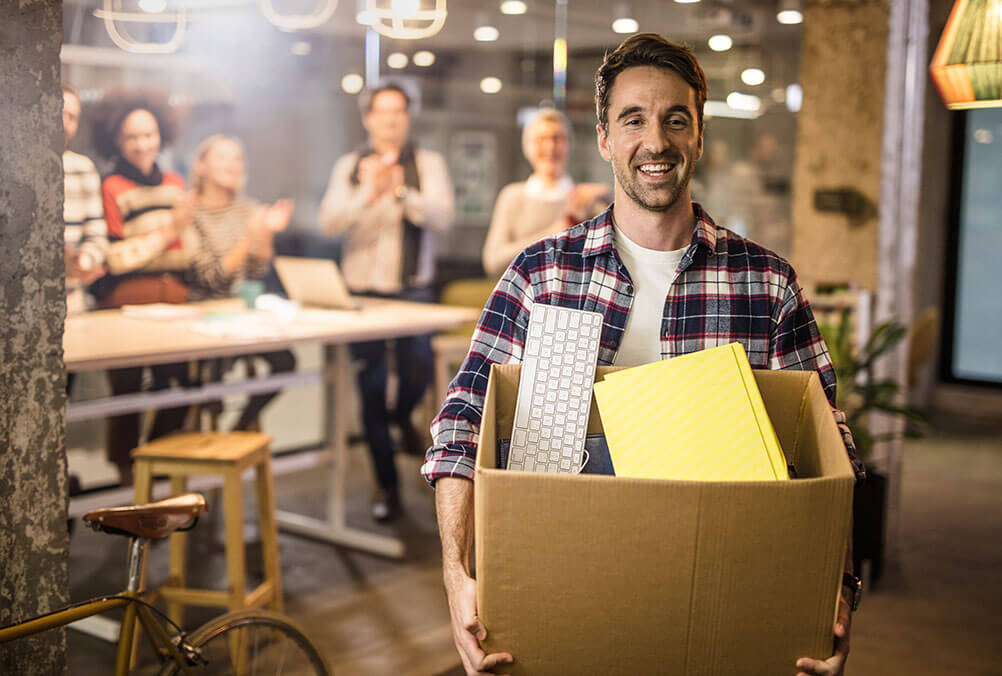 Would You Quit Your Job if You Won the Lottery? A smiling man carries a box of possessions out the door as he quits his job after winning the lottery