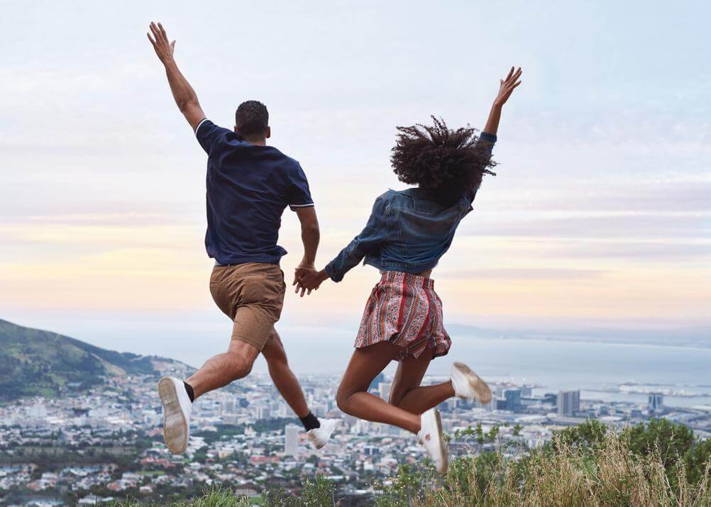 Happy couple holding hands jumping above Cape Town
