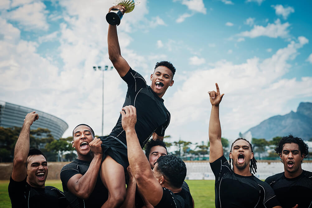 A rugby player celebrating victory on the shoulders of his teammates with a trophy in his hands