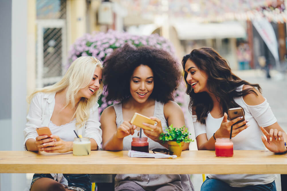 Three women sitting outside a bar reading a daily lotteries guide