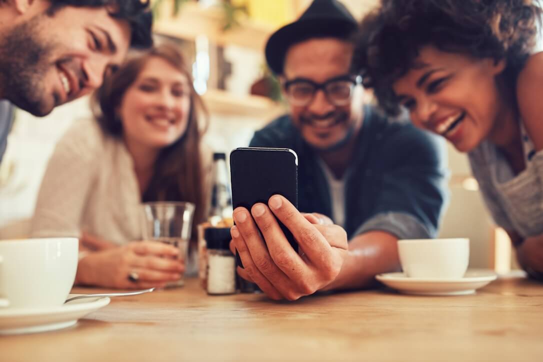 A group of friends in a coffee shop reading the SA Lotto Betting Guide on a mobile phone