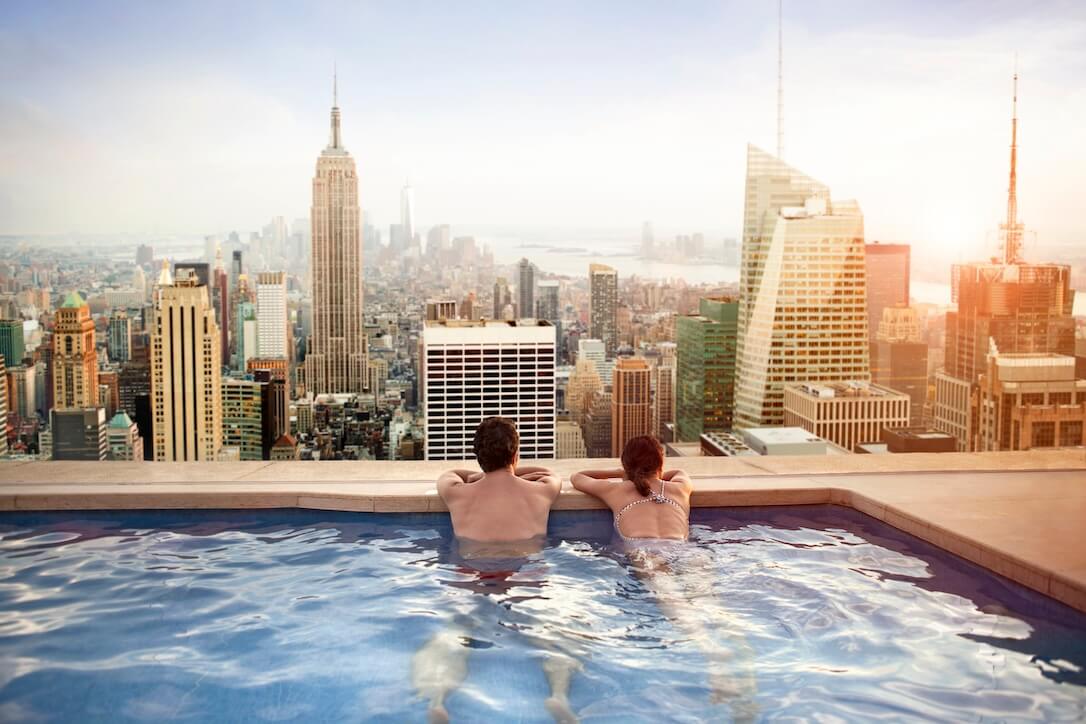A couple in a pool overlooking New York City, discussing how to bet on Mega Millions from South Africa.