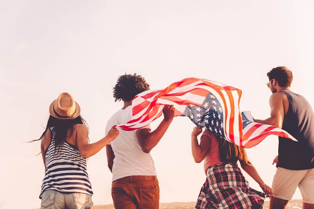 US PowerBall vs MegaMillions Four people on a beach with an American flag discussing the PowerBall vs MegaMillions debate